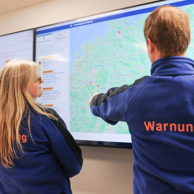 Zwei Personen stehen vor einem großen Bildschirm, der die Deutschland-Karte zeigt. Dies geschieht im Rahmen des bundesweiten Warntags.