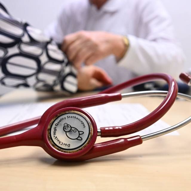 Ein Arzt misst in einer Bereitschaftspraxis in einem Krankenhaus in einem Untersuchungsraum bei einer Patientin den Blutdruck (gestellte Szene). Im Vordergrund liegt ein Stethoskop. (zu dpa: «Bürgermeister laufen Sturm gegen Pläne zu Notfallpraxen»)