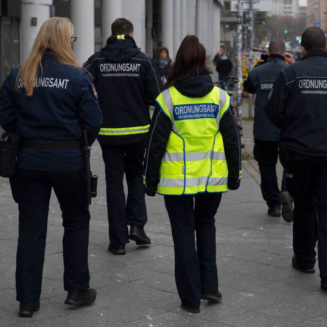 Städtische Mitarbeiter werden von Sicherheitskräften zu einem Termin begleitet.