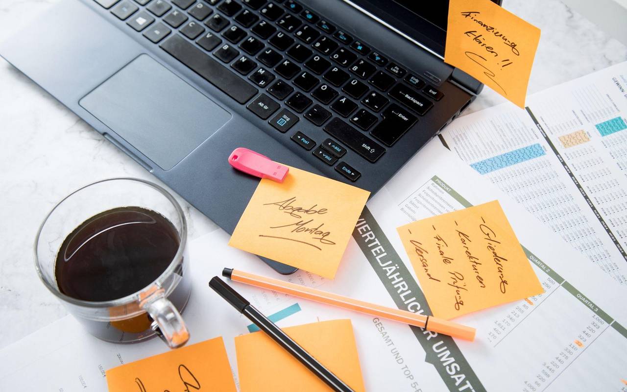 Chaos auf dem Schreibtisch mit Laptop, USB-Stick und Notizen