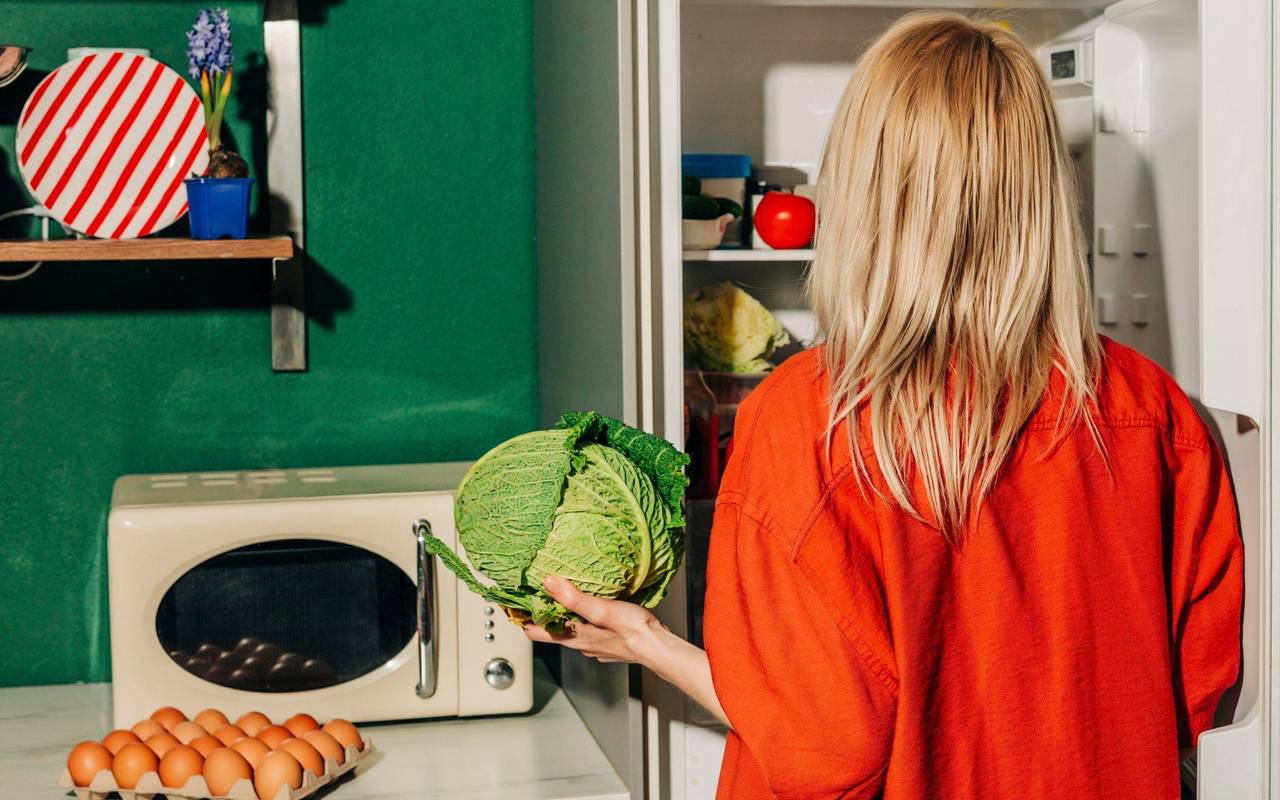 Eine Frau hält einen Kohl vor einem offenen Kühlschrank