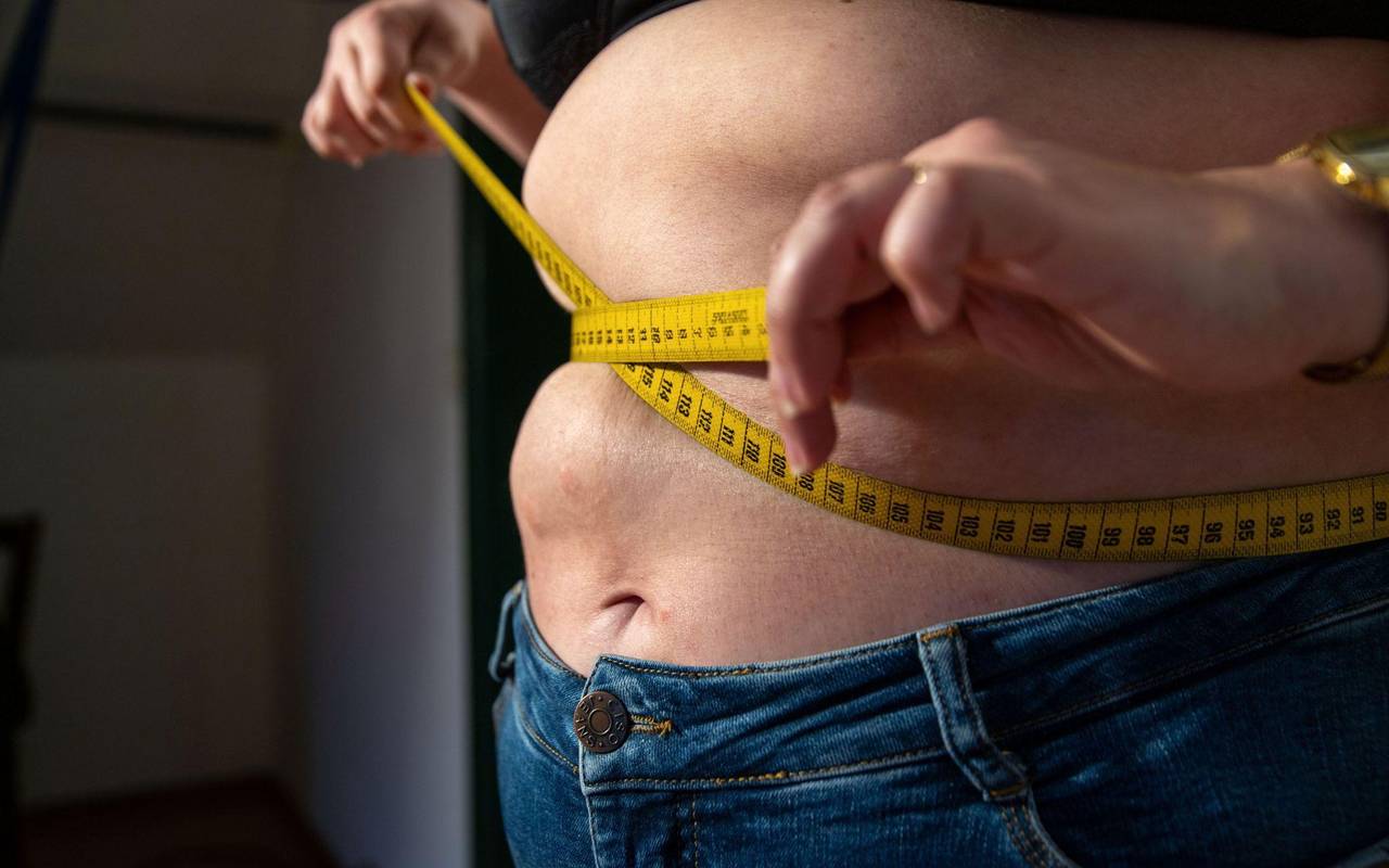 Eine Frau mit Übergewicht hält ein Maßband um ihren Bauch.