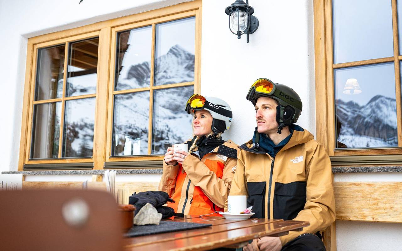 zwei Skifahrer machen vor einer Berghütte eine Pause
