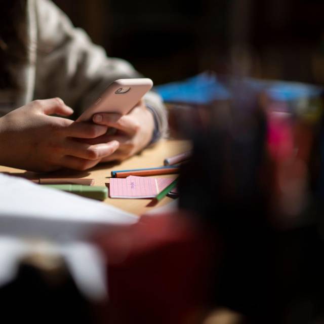 Eine Jugendliche sitzt mit Smartphone an einem Schreibtisch