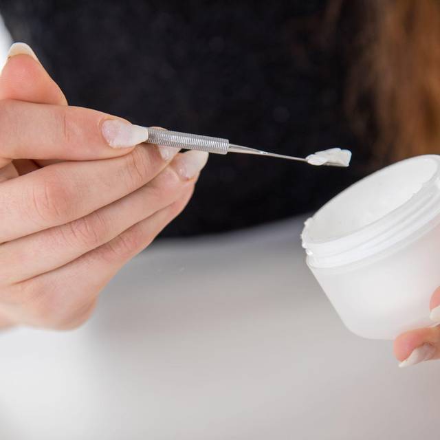 Eine Frau entnimmt mit einem Spatel Creme aus einem Tiegel