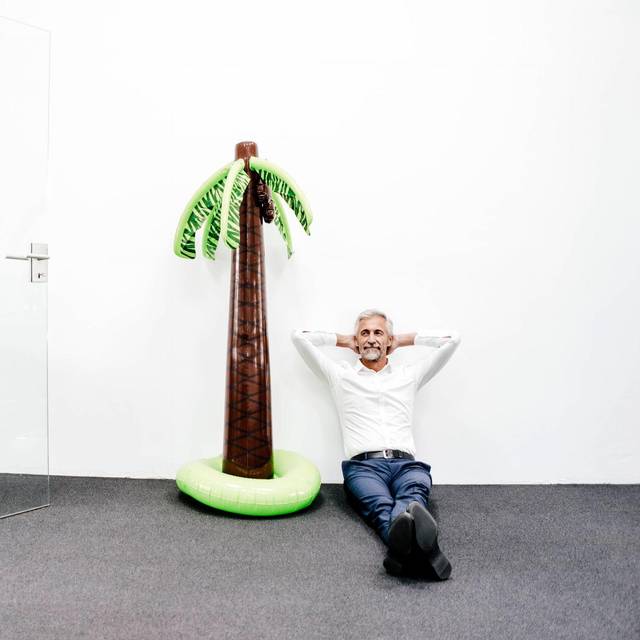 Mann sitzt im Büro neben einer aufblasbaren Palme