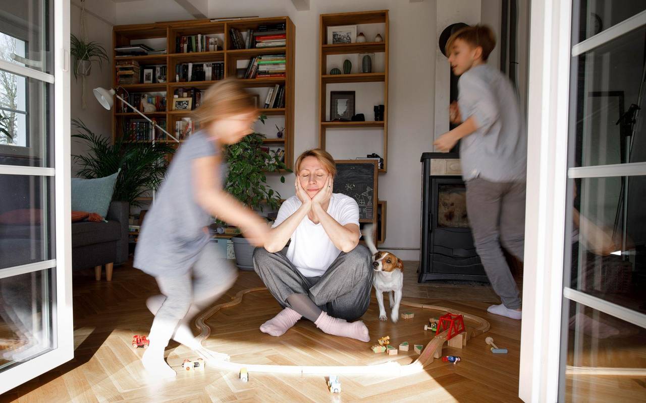 Gestresste Mutter sitzt zwischen dem Spielzeug ihrer Kinder