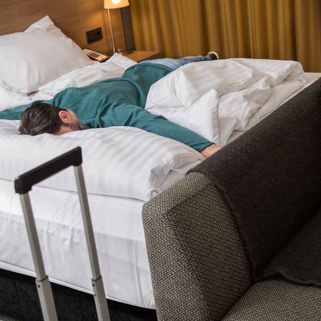 Ein Mann liegt erschöpft auf einem Bett in einem Hotelzimmer