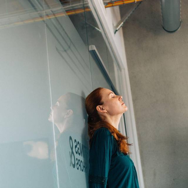 Eine junge Frau lehnt nachdenklich an einer Glaswand