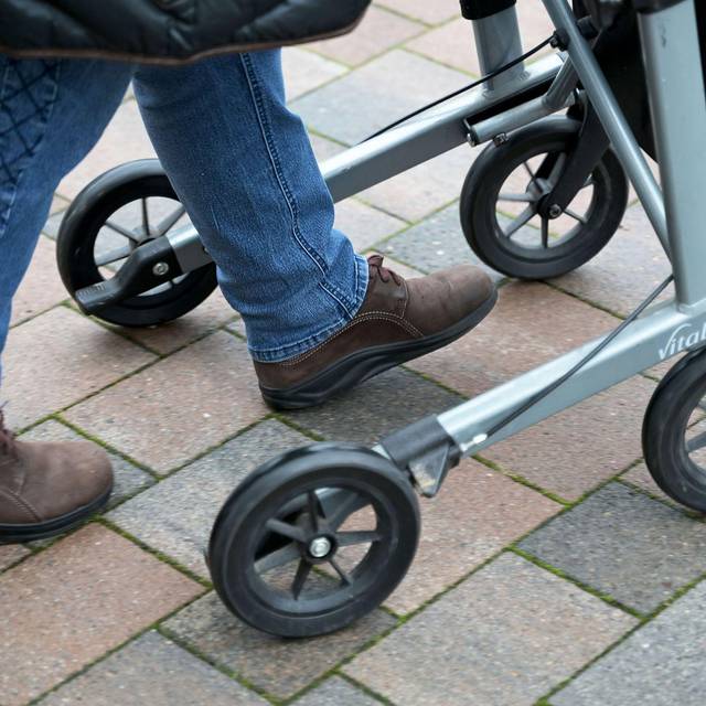 Seniorin fährt mit ihrem Rollator auf einem gepflasterten Weg