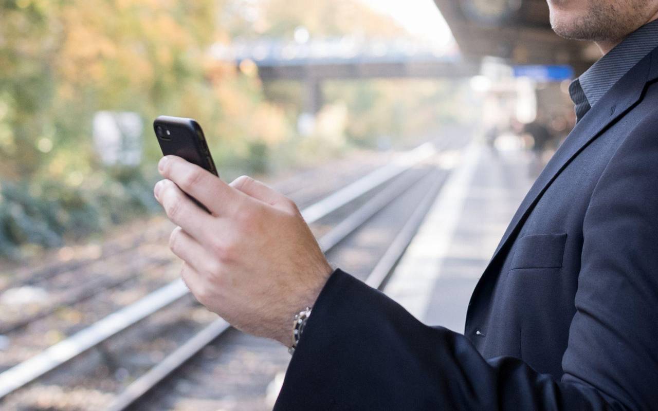 Mann mit Smartphone am Gleis