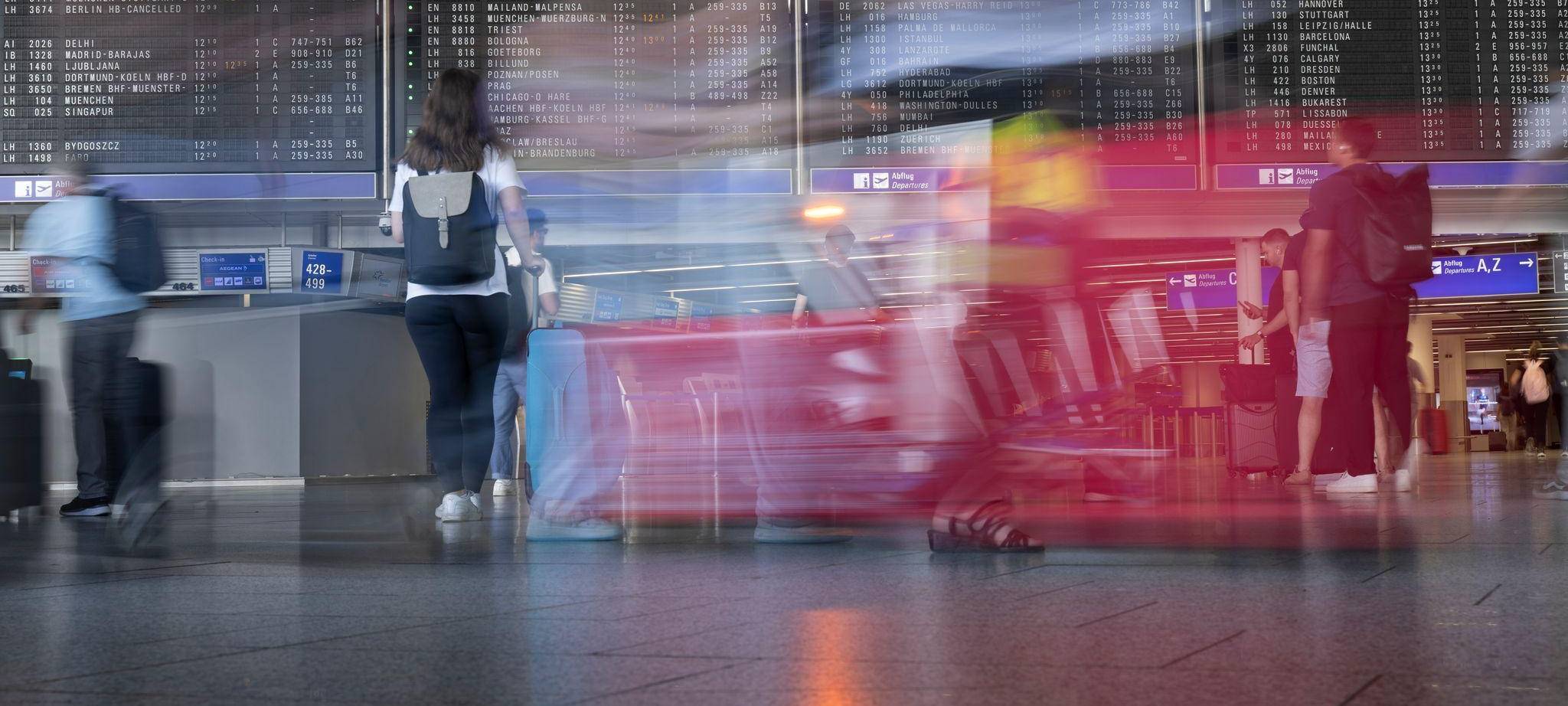 Passagiere gehen vor der Anzeigetafel im Flughafen entlang