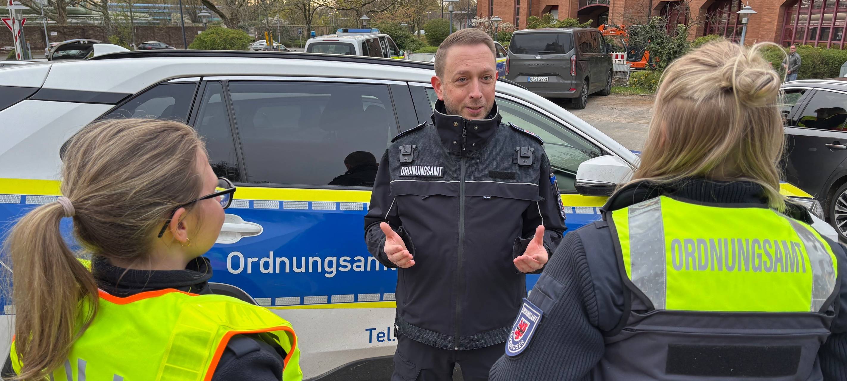 Vor dem Gebäude des Wiesdorfer Treff steht ein Auto des Leverkusener Ordnungsamts. Davor steht Marcus Richter, der Leiter des Ordnungsdienstes. Er unterhält sich gestikulierend mit Einsatzkräften des Ordnungsamts und des Zoll.