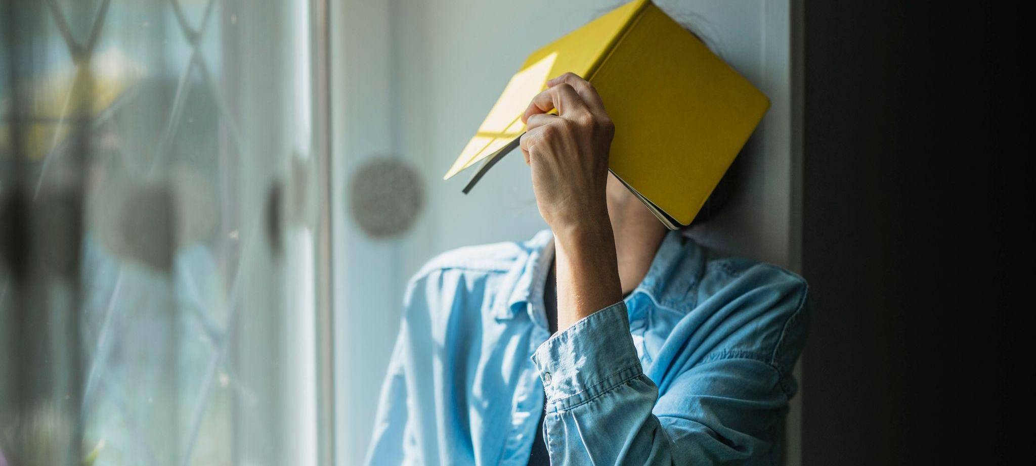 Eine Frau verbirgt ihr Gesicht hinter einem Notizheft
