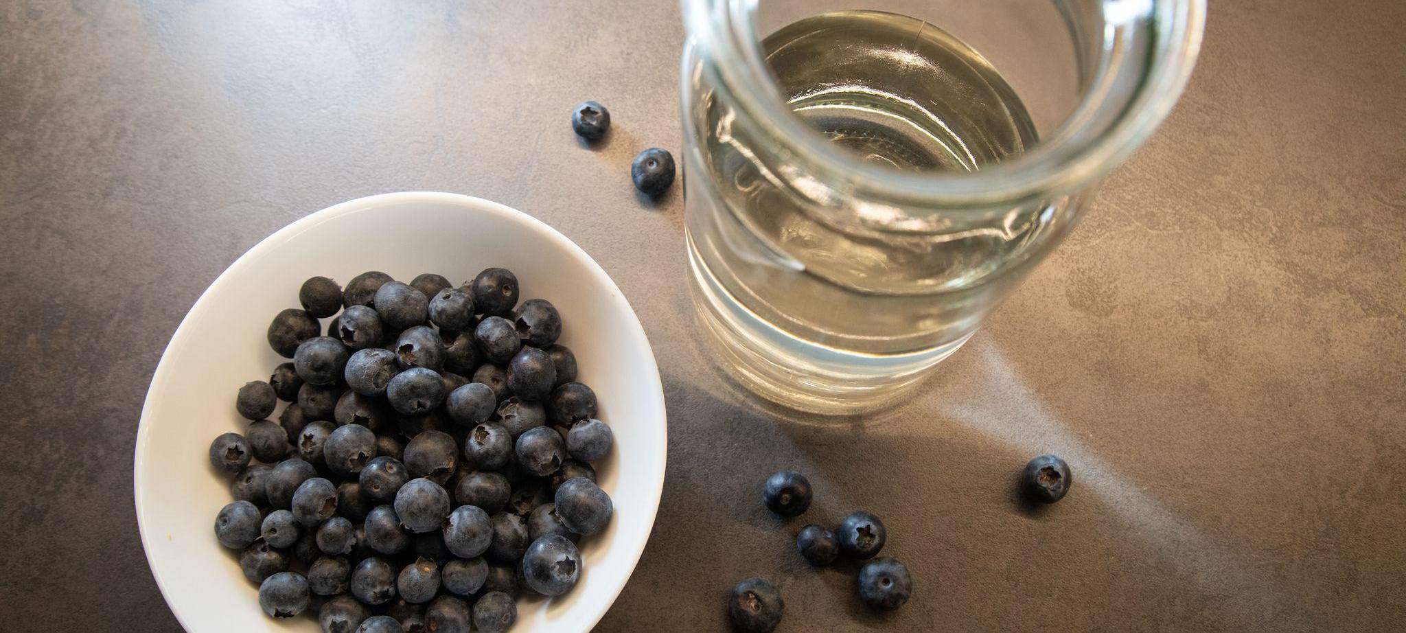 Blaubeeren liegen in einer Schale neben einem Glas Wasser