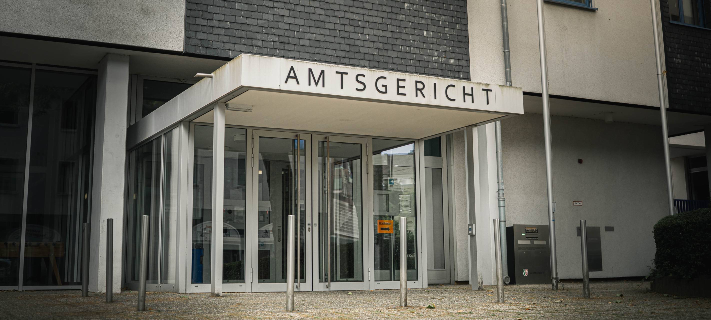 Eingangsbereich des Amtsgerichts Leverkusen mit verglastem Vorbau und dem Schriftzug „Amtsgericht“ über der Tür.