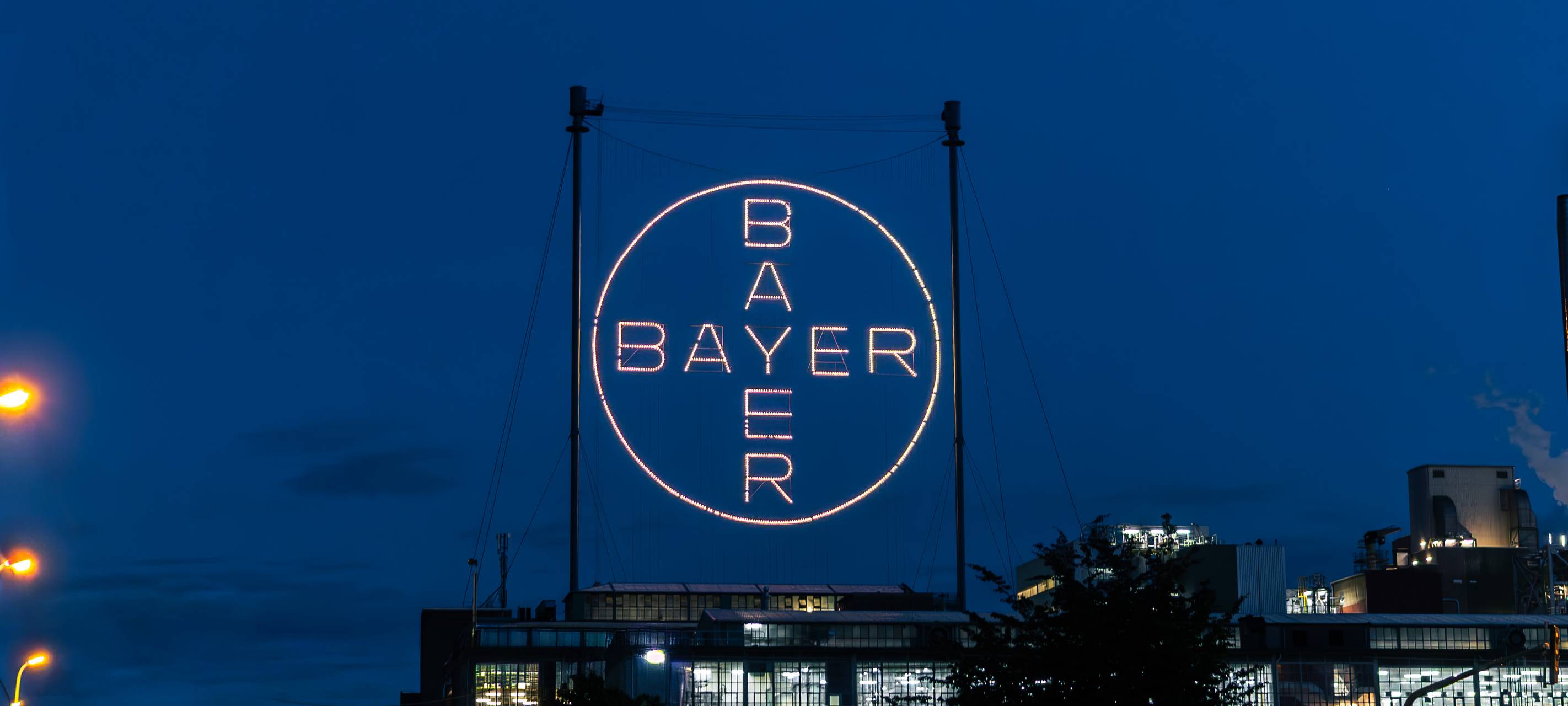 Beleuchtetes Bayer-Kreuz bei Nacht über dem Werksgelände des Chempark Leverkusen
