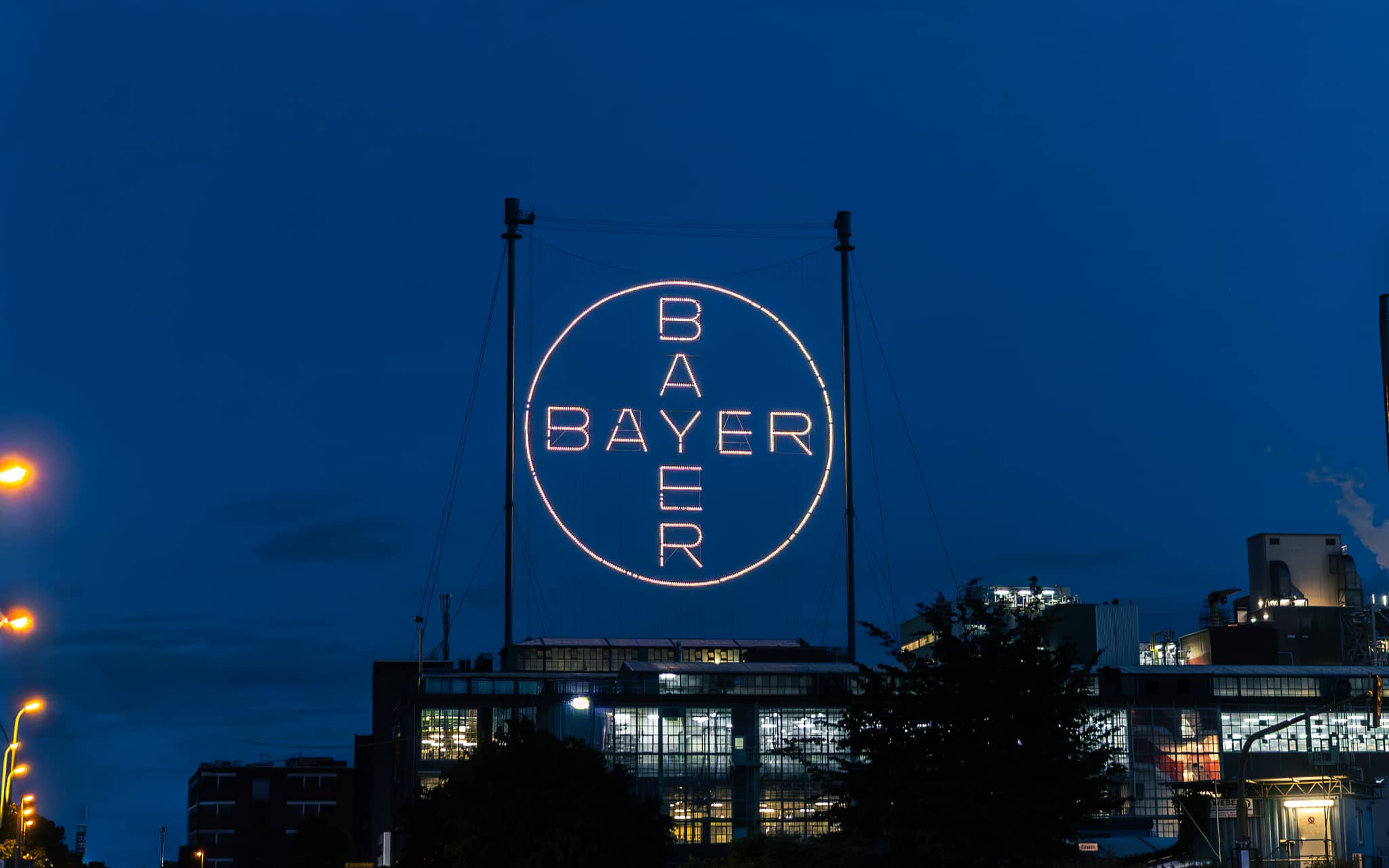 Beleuchtetes Bayer-Kreuz bei Nacht über dem Werksgelände des Chempark Leverkusen