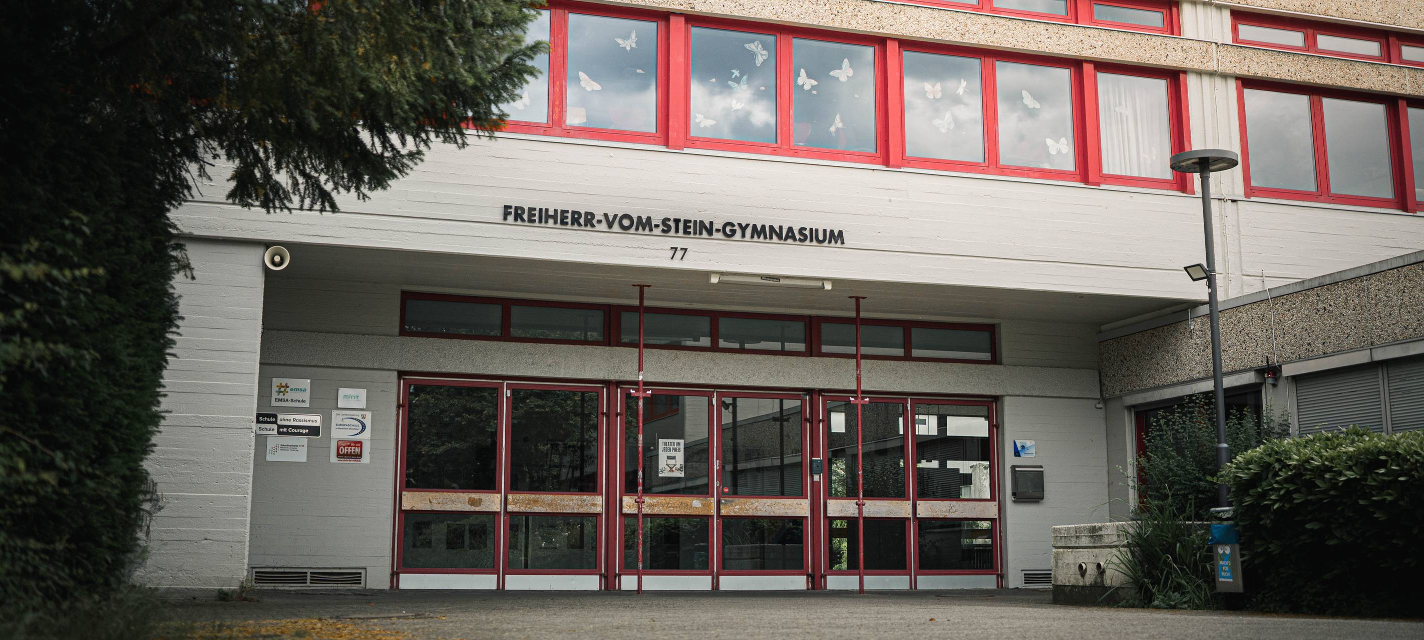 Eingangsbereich des Freiherr-vom-Stein-Gymnasiums mit rotem Fensterrahmen und Schulnamen über dem Eingang.