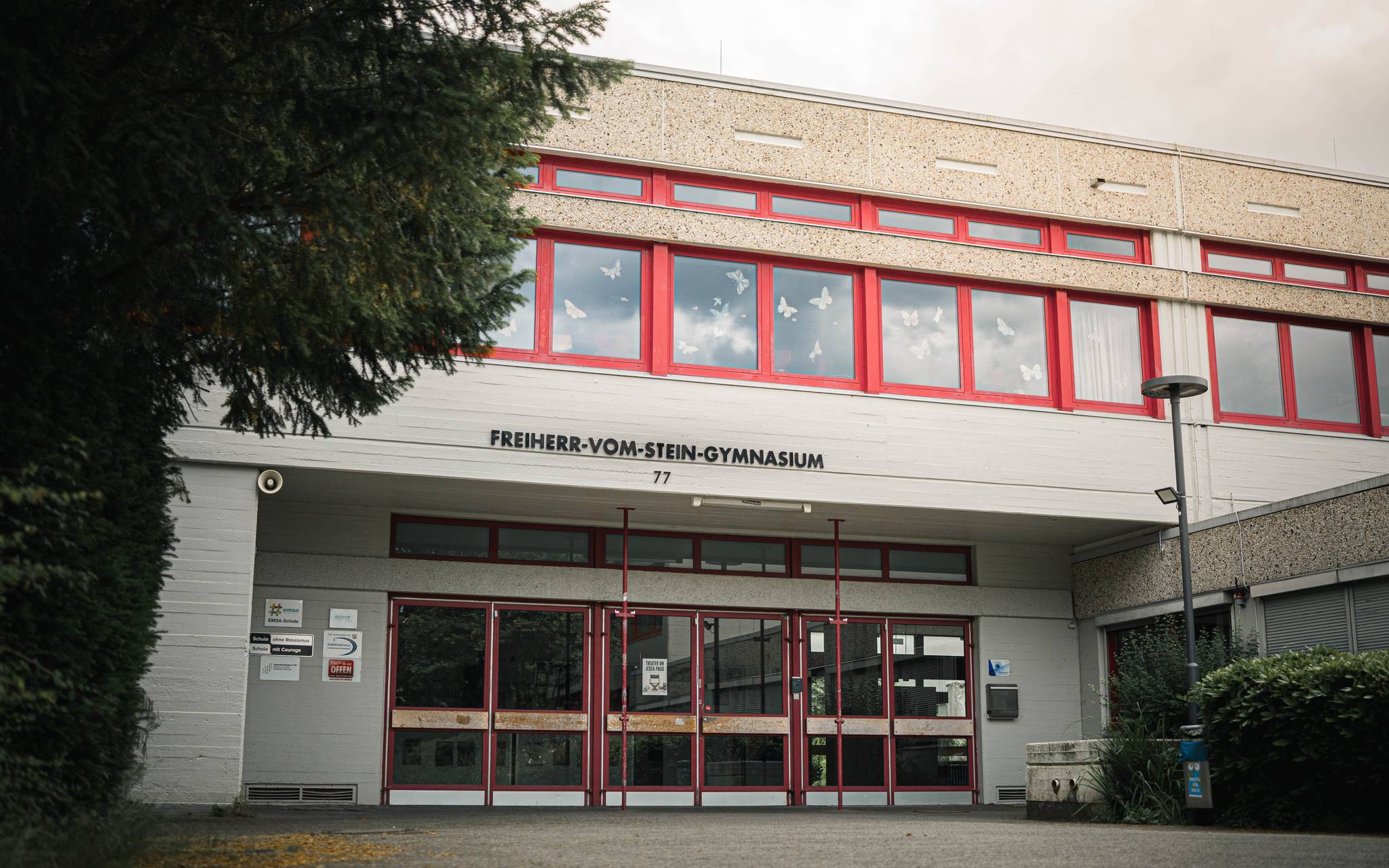 Eingangsbereich des Freiherr-vom-Stein-Gymnasiums mit rotem Fensterrahmen und Schulnamen über dem Eingang.