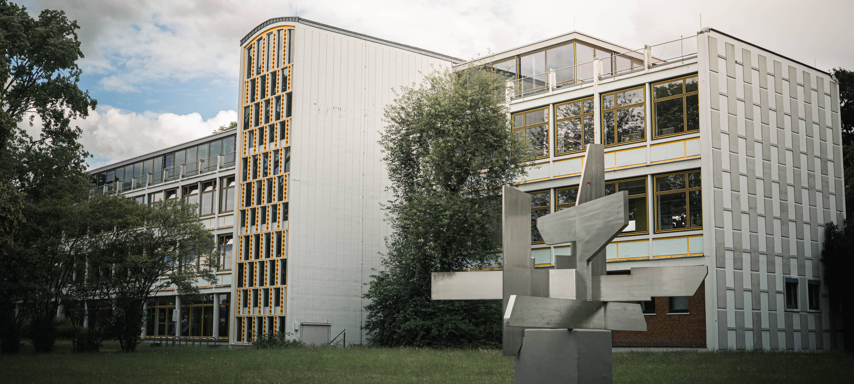 Gebäude des Geschwister-Scholl-Berufskollegs mit Wiese und einer Skulptur im Vordergrund.
