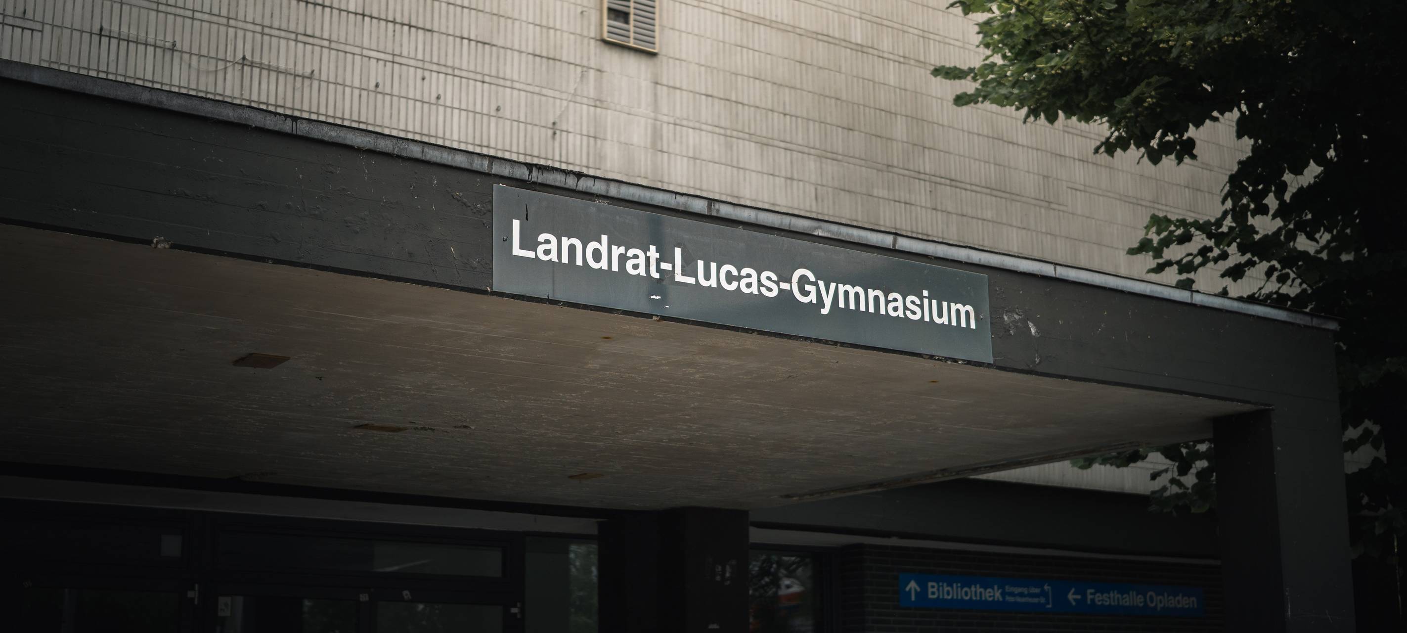 Eingangsbereich des Landrat-Lucas-Gymnasiums mit Namensschild über dem Vordach.