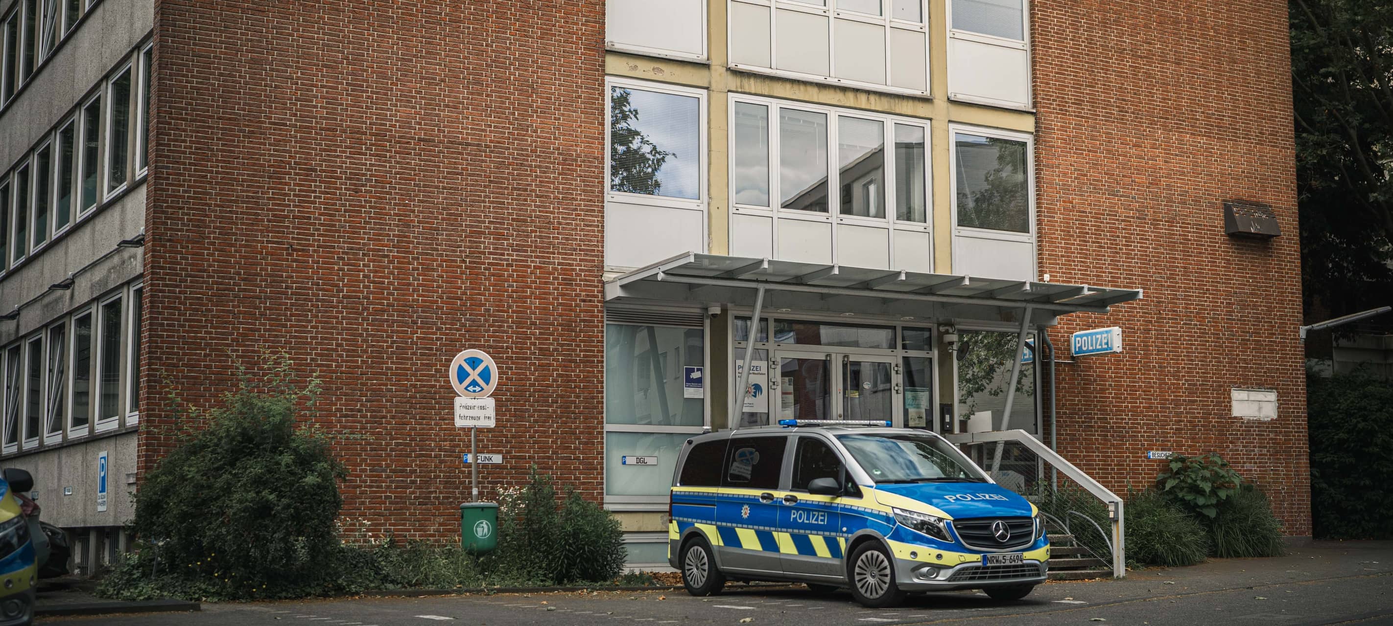 Polizeiwache Opladen mit Eingangsbereich und geparktem Polizeifahrzeug vor dem Gebäude.