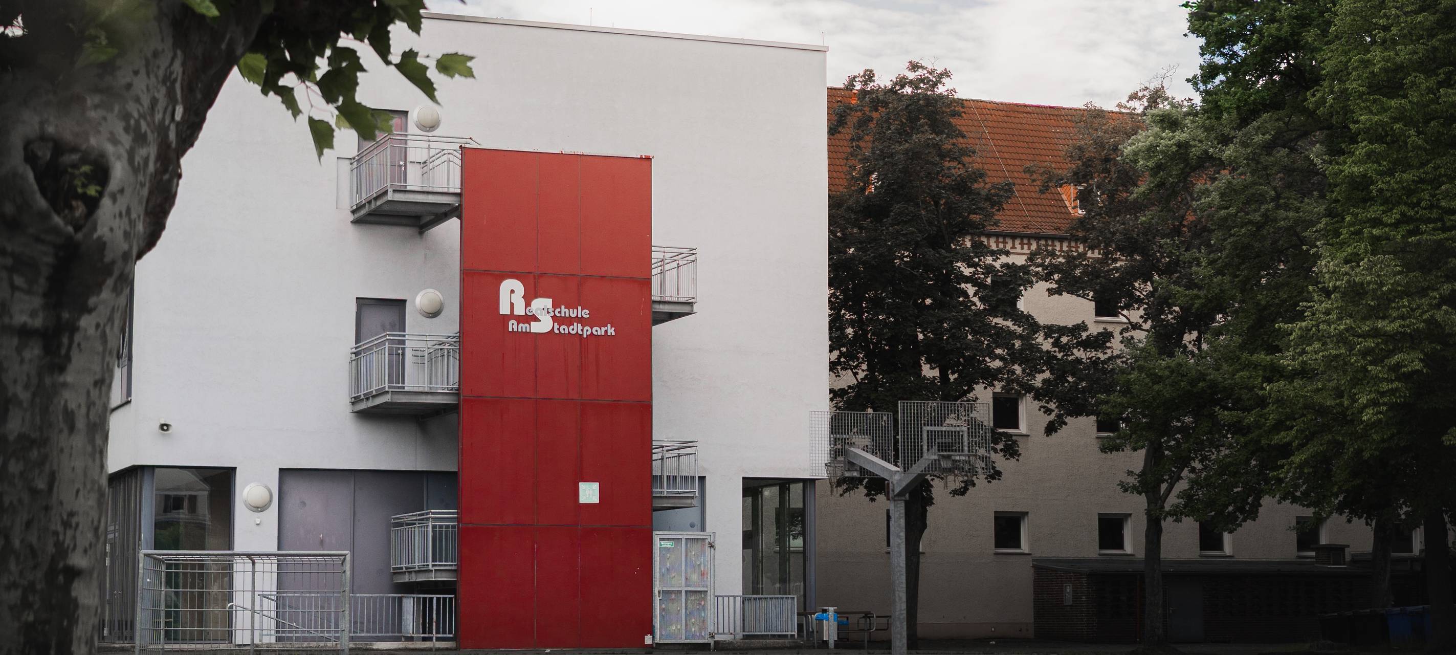 Gebäude der Realschule am Stadtpark mit rotem Fassadenelement und Schulnamen an der Front.