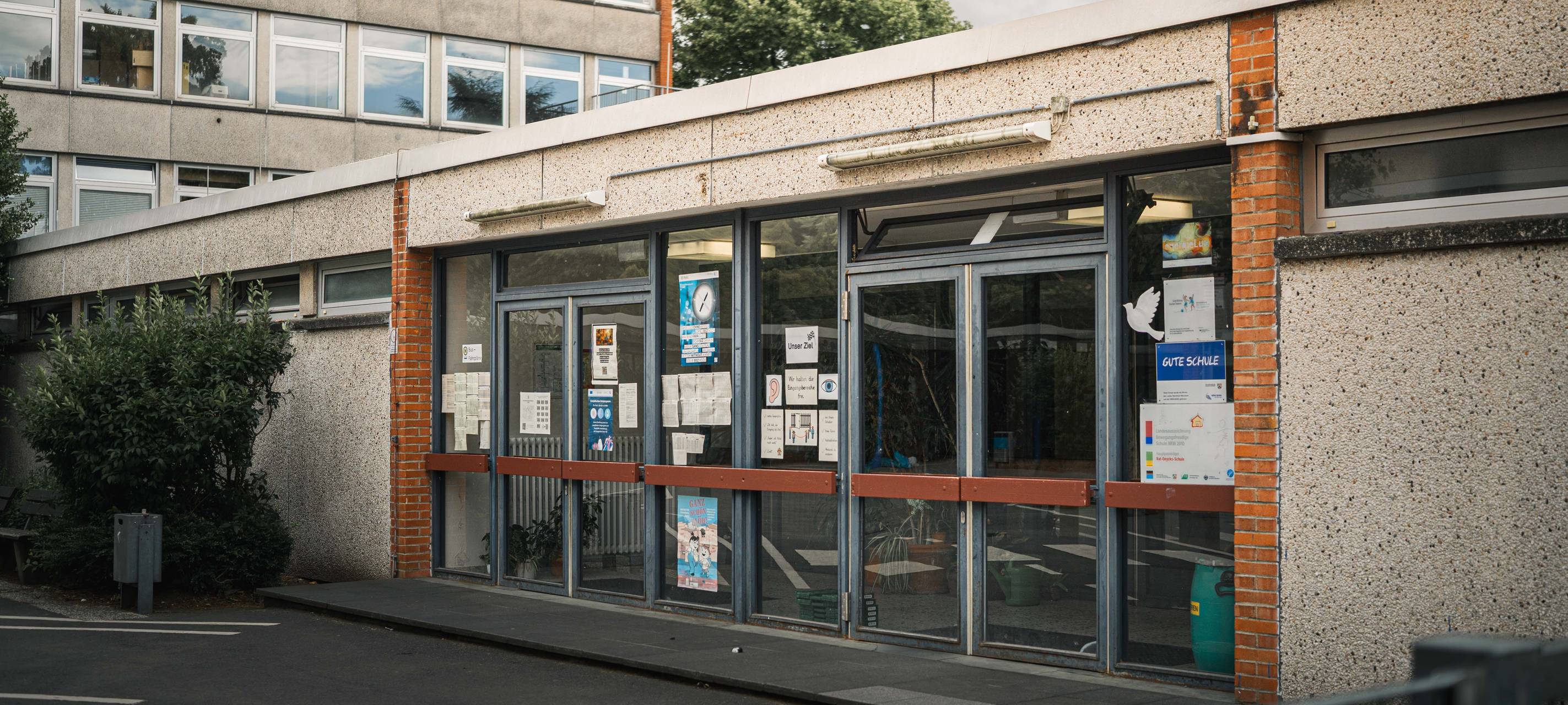 Eingangsbereich der Schule an der Wupper mit verglasten Türen und Aushängen an der Fassade.