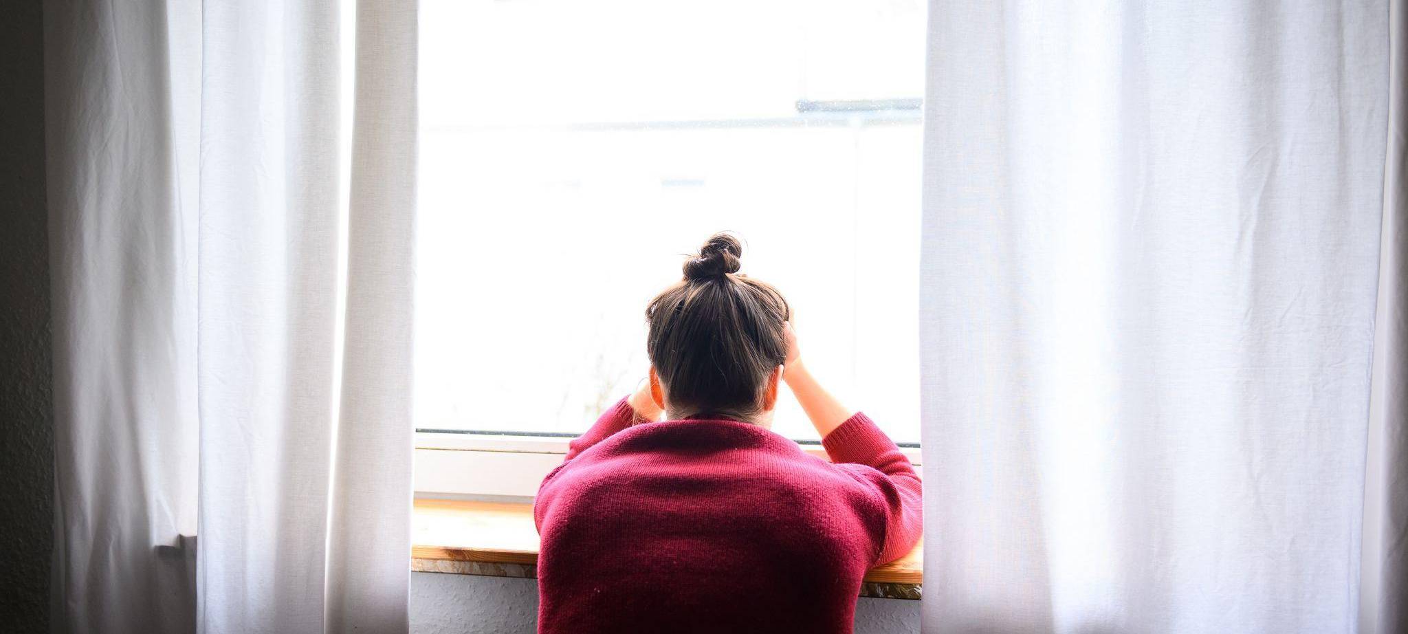 Eine Person an einem Fenster nimmt den Kopf in die Hände