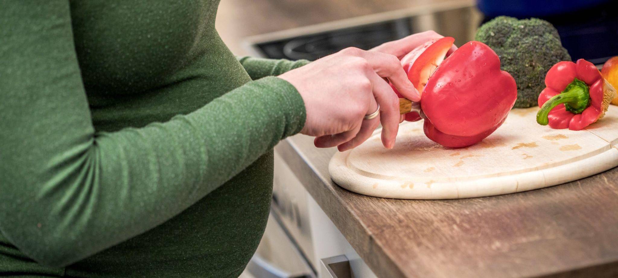 Eine schwangere Frau schneidet sich frisches Gemüse